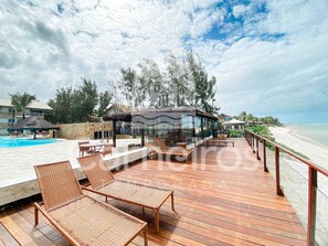 A wooden deck with lounge chairs, a pool, and a beach view. - Marupiara Muro Alto (Ipojuca)