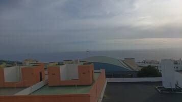 Una azotea con edificios al fondo, cielo despejado y vista distante del mar.