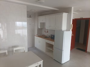 A compact kitchen with white cabinets, a sink, and a refrigerator. There is a dining table with chairs.