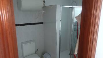 Un baño con inodoro, cabina de ducha y soporte para papel higiénico.