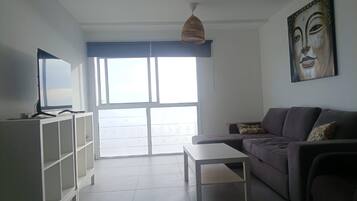 Una sala de estar con un sofá, una mesa de centro, un televisor sobre un mueble bajo y un ventanal grande.