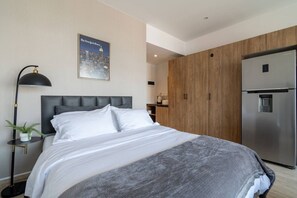 Ein modernes Hotelzimmer mit einem Bett, einem Nachttisch, einer Lampe, einem Poster, einem Kleiderschrank und einem Kühlschrank.