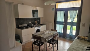 A compact kitchen with a dining table, chairs, and a view through a door with curtains. - Vrbo Property (Emilia-Romagna)