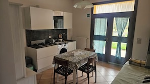 Cozinha compacta com mesa de jantar, cadeiras e vista através de uma porta com cortinas.