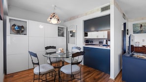 A compact kitchen with a dining area, featuring a round glass table, four chairs, and a decorative hanging light fixture. - Amazing location at Indian Springs Colony 30-day minimum stay (Largo)