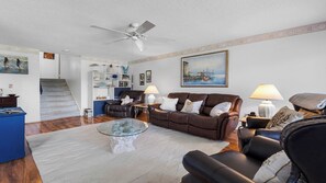 A living room with a brown leather sofa, a glass coffee table, a bookshelf, a painting, and a ceiling fan. - Amazing location at Indian Springs Colony 30-day minimum stay (Largo)