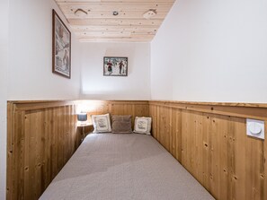 Ein Zimmer mit einem Holzbett, einem gerahmten Bild an der Wand und einem kleinen Nachttisch mit einer Lampe.