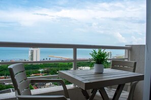 A balcony with a table and chairs, overlooking a coastal view with buildings and greenery. - APARTMENT IN THE LOTUS BUILDING (Cartagena de Indias)