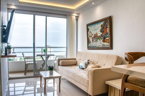 Un salon moderne avec un canapé, une table à manger et des chaises. Une grande fenêtre offre une vue sur la mer.