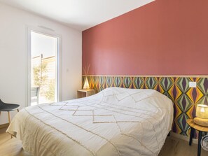 Ein Schlafzimmer mit einem Bett, einem Sessel, einem Nachttisch mit Lampe und einem Fenster.