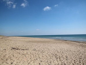 Uma extensa praia de areia com ondas suaves, céu claro e horizonte distante.