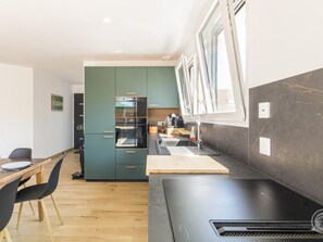 A modern kitchen with a built-in oven, a sink, and a window with blinds. - House near beach - 6 guests (Saint-Jean-de-la-Rivière)