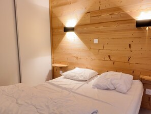 A bedroom with a wooden headboard, a bed with white bedding, and two bedside tables with lamps. - Bright apartment near slopes - 6 guests (Villarodin-Bourget)