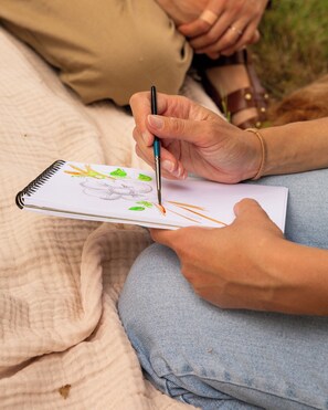 Une personne tenant un carnet de croquis et un crayon, en train de dessiner une illustration de plante sur une page.
