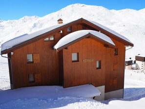 Eine Holzhütte mit schneebedecktem Dach in einer verschneiten Berglandschaft.