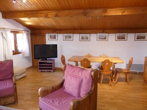 A cozy room with a wooden ceiling, a television on a stand, a dining table with chairs, and a sofa with a checkered cushion. - Cozy apartment in the center - 6 guests (Pralognan-la-Vanoise)