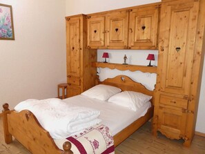 A wooden bed with a headboard, a nightstand, and a small table. - Cozy apartment in the center - 6 guests (Pralognan-la-Vanoise)