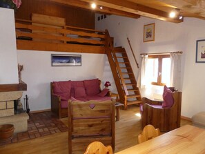 A cozy room with a wooden staircase, a sofa, a dining table, and a fireplace. - Cozy apartment in the center - 6 guests (Pralognan-la-Vanoise)