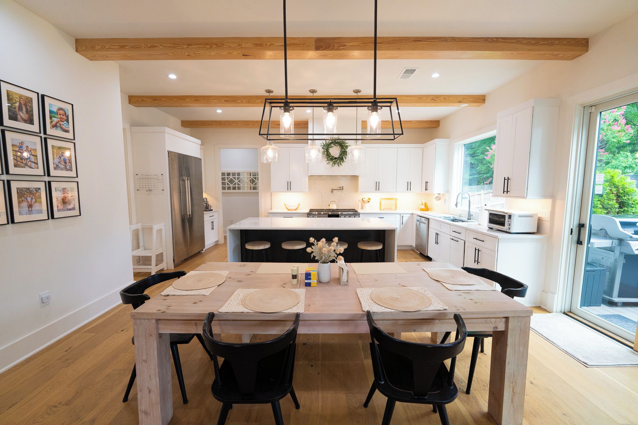 Una cocina moderna con una isla central, iluminación colgante y un comedor con mesa y sillas de madera.