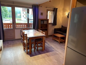 Ein gemütlicher Wohnbereich mit Esstisch, Stühlen, einer Couch, einem Bücherregal und einem Kühlschrank.