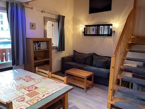 A cozy living room with a sofa, a wooden table, a bookshelf, and a staircase. - Apartment in the heart of the resort - 6 guests (Pralognan-la-Vanoise)