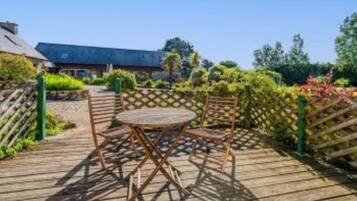 An outdoor wooden deck with a table and chairs, surrounded by greenery and a fence.