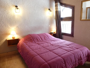 Un dormitorio con cama, dos lámparas de noche, una ventana con cortinas y un aplique de pared.
