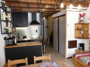 Eine kleine Küche mit Holzarbeitsplatte, schwarzen Schränken und einem modernen Herd. Es gibt einen Essbereich mit Holztisch und Stühlen sowie eine gemütliche Ecke mit einem Bett und einem Regal mit Dekoration.