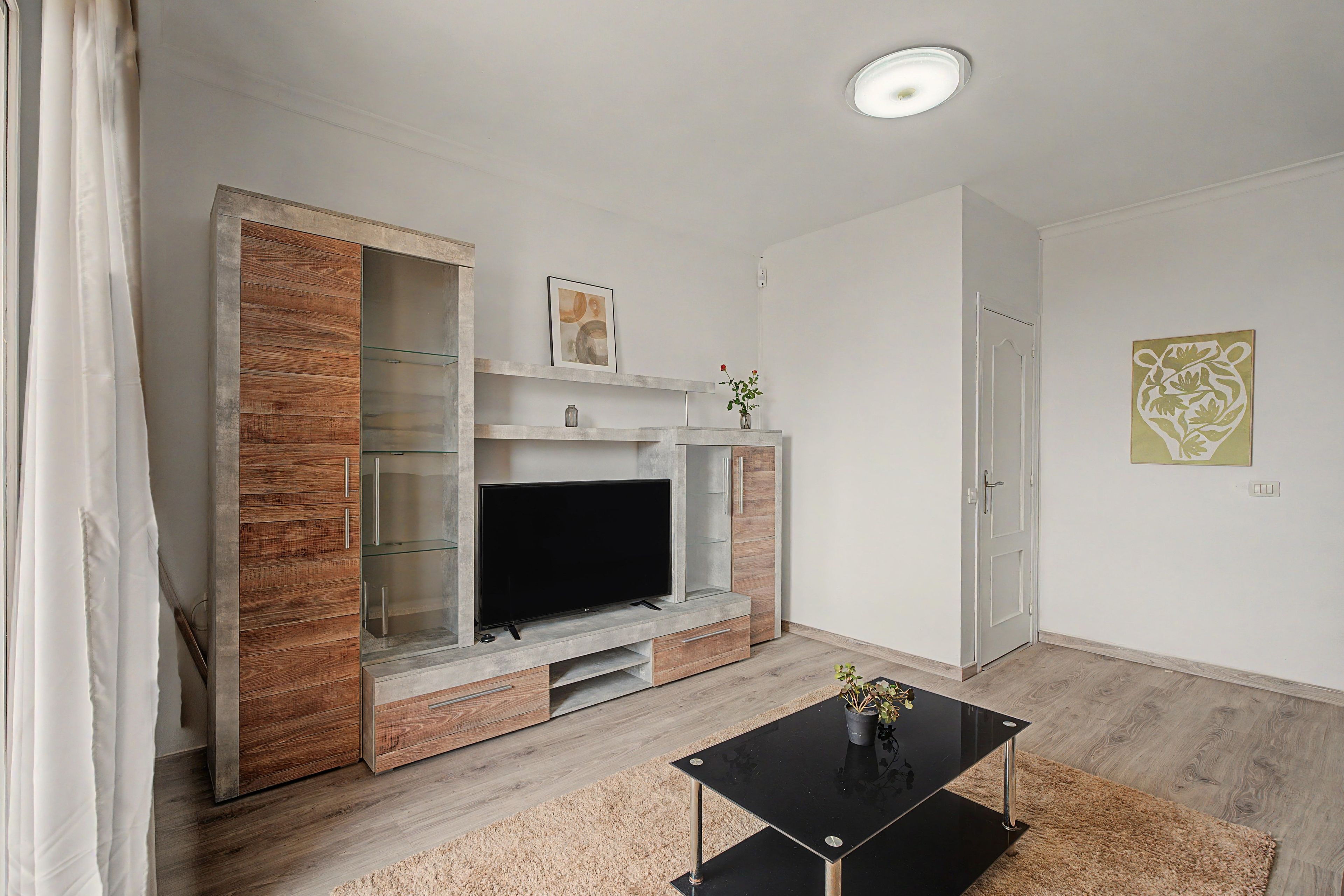 Una sala de estar moderna con una televisión de pantalla plana, armarios de madera, una mesa de centro de vidrio y una decoración minimalista.