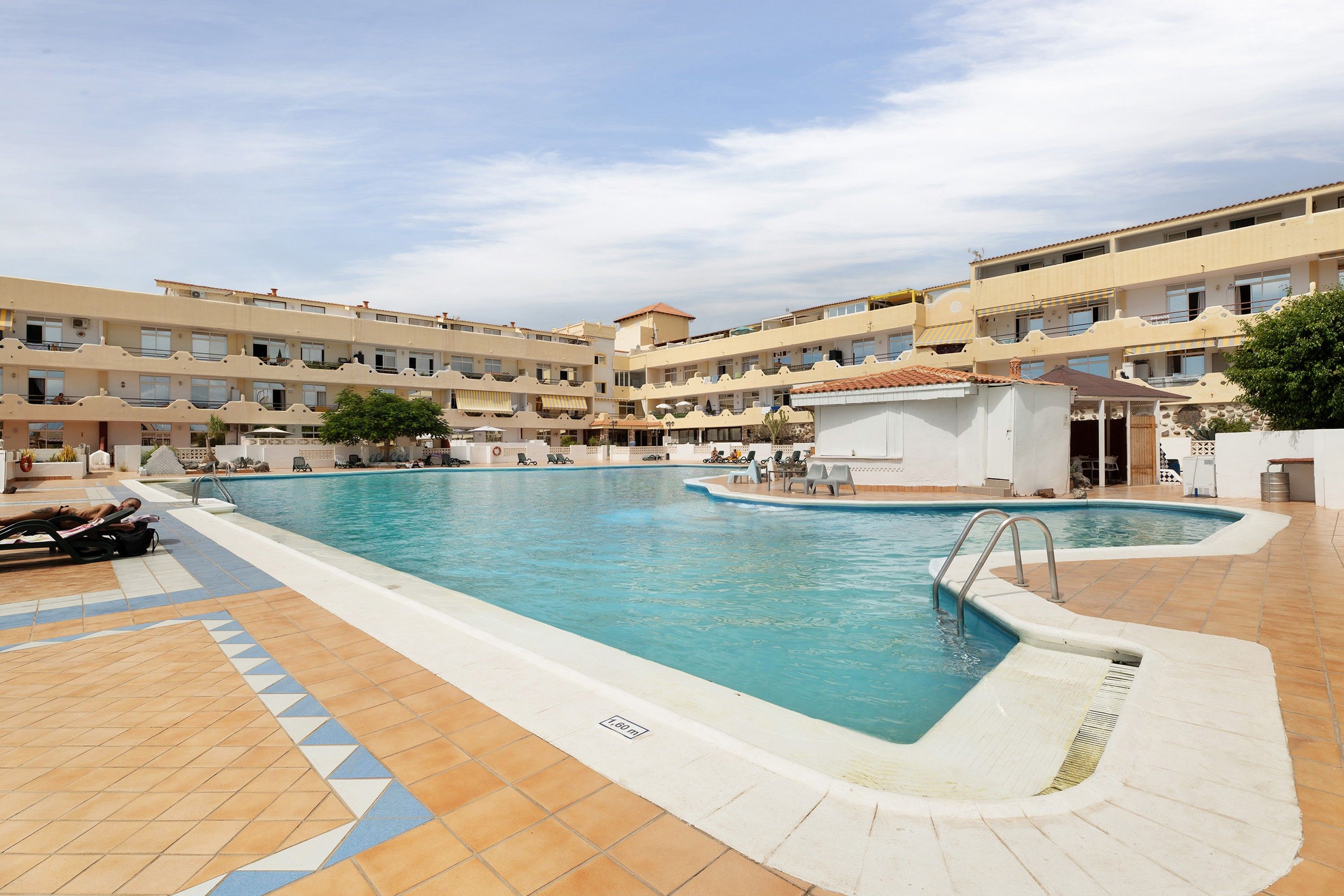 Zona de piscina de hotel con varias piscinas, tumbonas y un área de estar cubierta.