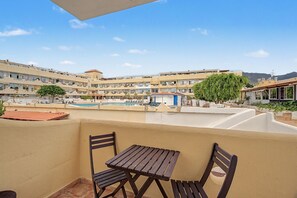 Un balcón con una mesa y sillas, con vista a una piscina y un conjunto de edificios.