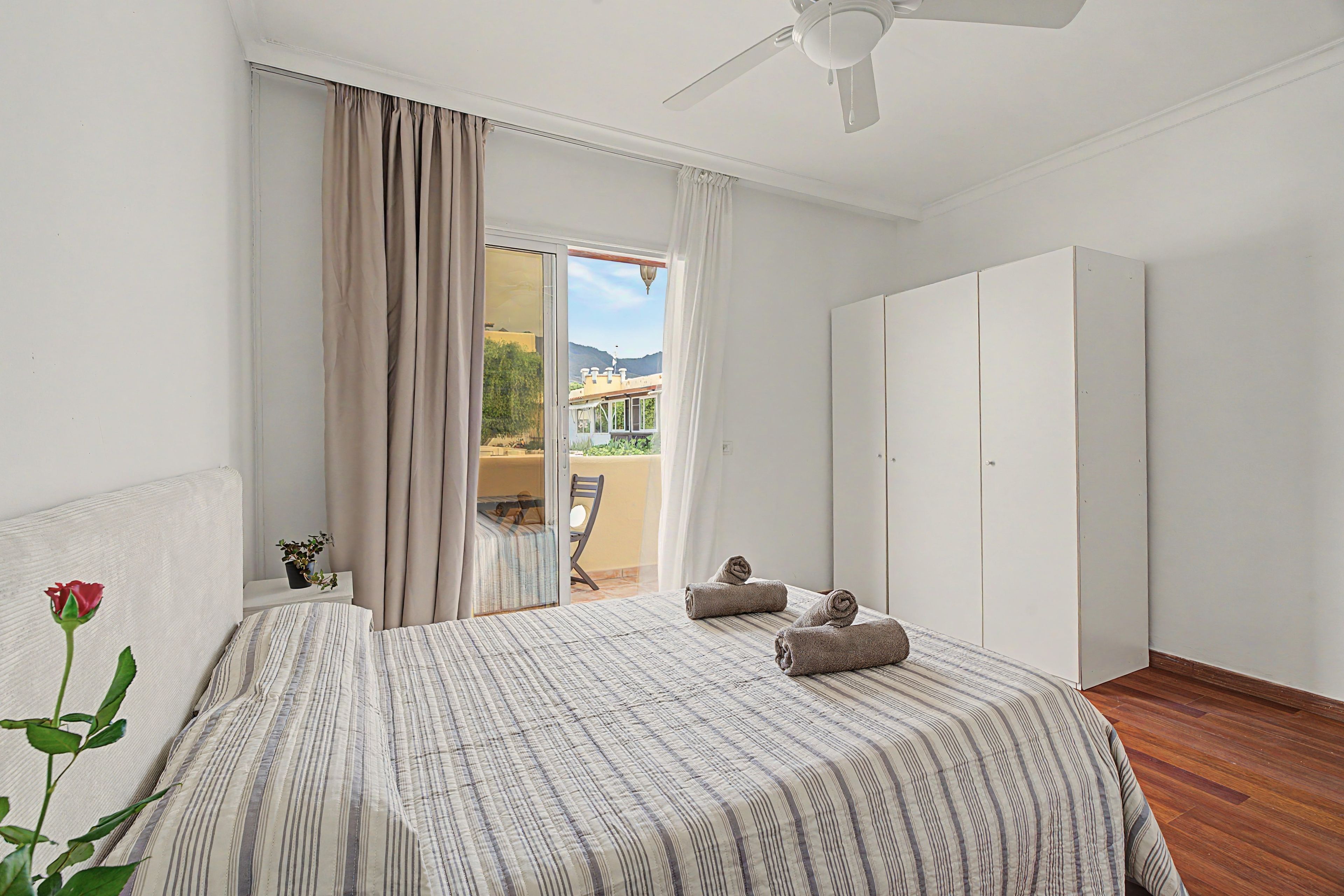 Un dormitorio con cama, una silla, armario y balcón con vistas a las montañas.