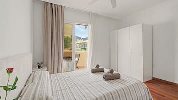 Un dormitorio con cama, una silla, armario y balcón con vistas a las montañas.