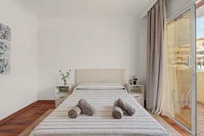 Un dormitorio con una cama, dos mesitas de noche, una ventana con cortinas y vistas a edificios.
