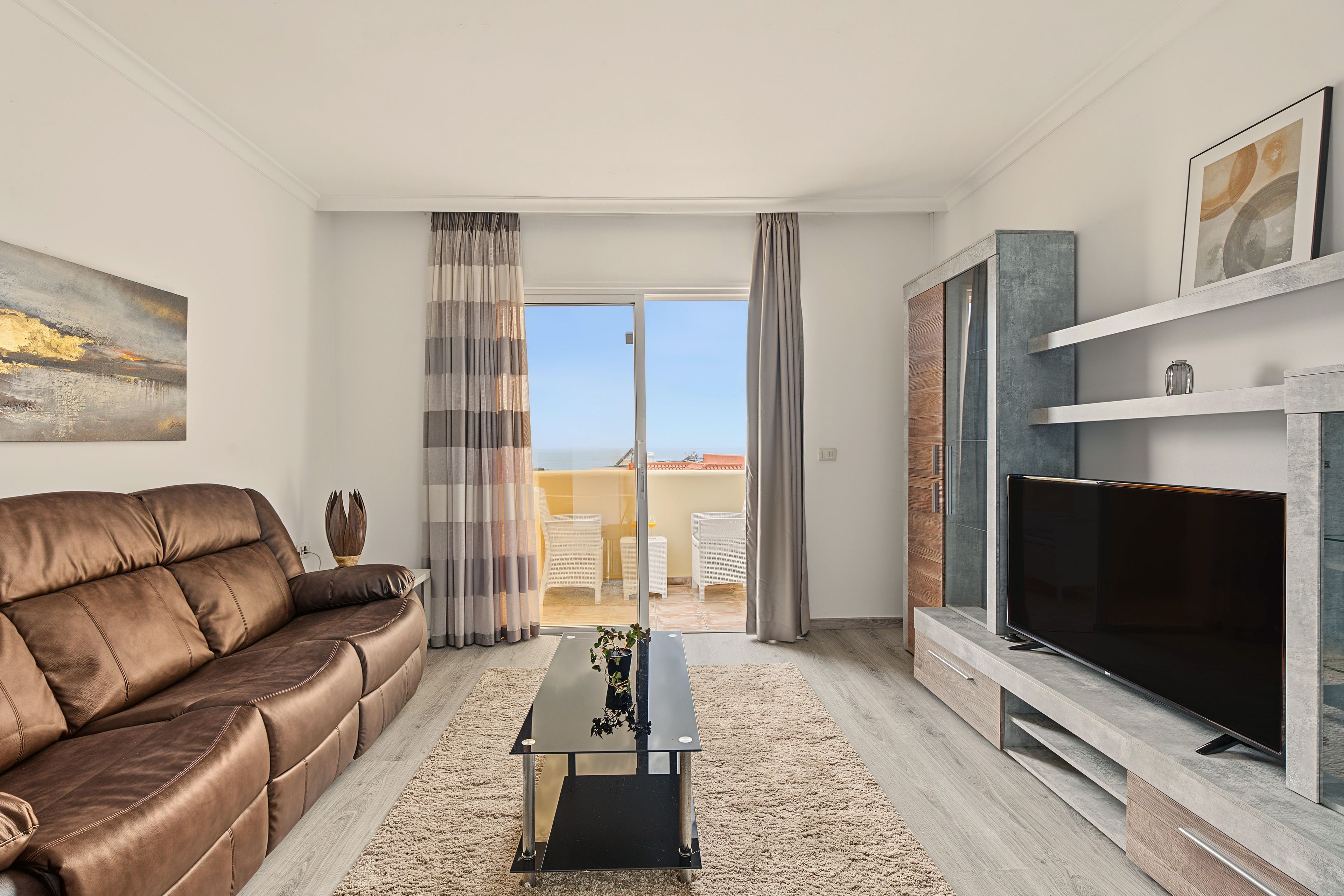 Una sala de estar moderna con un sofá de cuero, un televisor de pantalla plana y un balcón con mobiliario exterior.