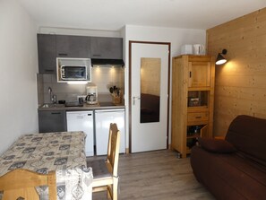 Cozinha compacta com eletrodomésticos modernos, área de jantar com toalha de mesa estampada e armário de madeira com espelho.