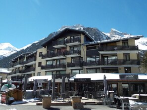 A multi-story hotel with balconies, outdoor seating, and a mountain backdrop. - Chalet in city center - 8 guests (Pralognan-la-Vanoise)