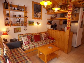 A cozy living room with a sofa, wooden shelves, a table, and a kitchen area. - Chalet in city center - 8 guests (Pralognan-la-Vanoise)