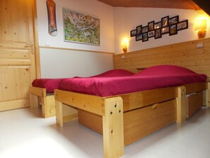 Ein hölzernes Bett mit einer roten Matratze in einem Raum, dessen Wände aus Holz sind und eine weiße Decke hat.