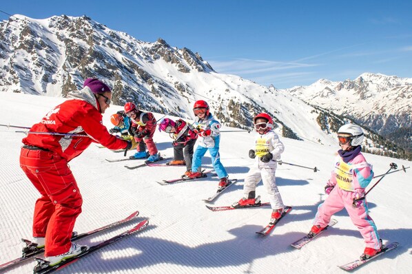 Eine Gruppe Kinder fährt auf einem verschneiten Hang mit einer gebirgigen Kulisse Ski.