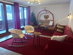 Sala de estar com um sofá vermelho, duas poltronas de balanço, uma mesa de madeira pequena e um pinheiro de Natal.