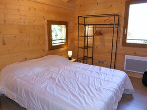 Quarto de cabana de madeira com cama, janela, prateleira e radiador.
