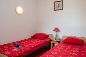 A room with two beds, each with a red bedspread and matching pillows. There is a wall-mounted light and a framed picture on the wall. - Au pied des pistes et du jardin des neiges (Villarodin-Bourget)