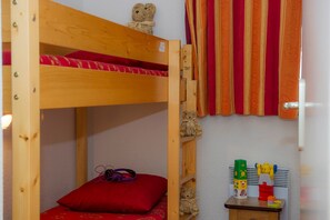 A bunk bed with a teddy bear on the top bunk, a red pillow, and a small table with toys and a pair of headphones. - Ski aux pieds | À 100m des commerces et du centre (Villarodin-Bourget)