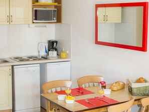 A compact kitchen with a microwave, coffee maker, and a dishwasher. There is a dining table with chairs and a red placemat. - Ski aux pieds |  À 100m des commerces et du centre (Villarodin-Bourget)