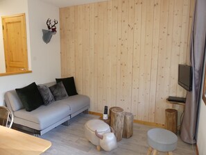 Ein modernes Wohnzimmer mit einer Couch, einem Hocker und einem Wandfernseher.