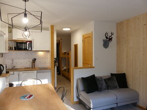 En kompakt opholdsstue med tekøkken, spiseplads og sofa.