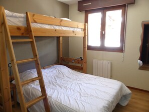 Ein Stockbett mit Holzlade, weißer Bettwäsche, einem Fenster mit Jalousien und einer Heizung.