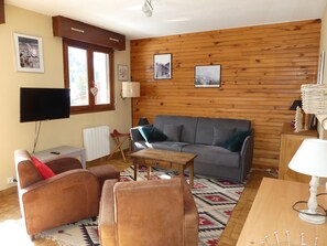 Ein gemütliches Wohnzimmer mit einer Couch, einem Sessel und einem an der Wand befestigten Fernseher.