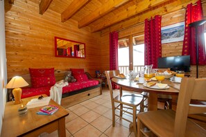 A cozy wooden cabin with a dining area, a sofa with red cushions, a television, and a breakfast setup. - Ski aux pieds | Proche du télésiège | Piscine (Saint-François-Longchamp)